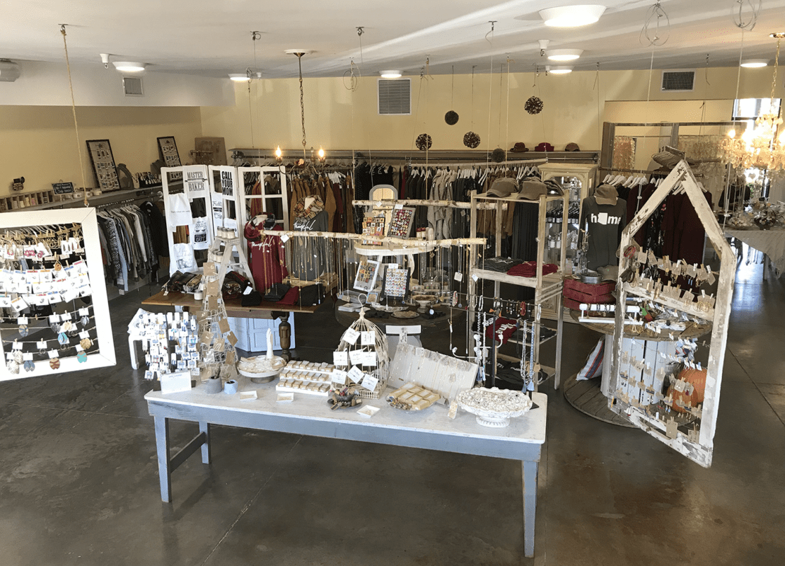 Interior of Poor Little Rich Girl located in Phoenix Arizona with a grey and white table with soaps, necklaces, earrings, clothing in the background on racks.